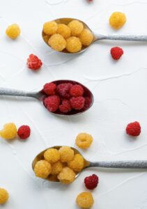 Vibrant display of fresh yellow and red raspberries on silver spoons in a flatlay style.